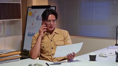 İşadamı geç saatlere kadar ofiste çalışıyor, masasında notlar alırken telefonla konuşuyor..