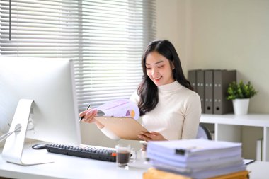 Kendine güvenen Asyalı ofis çalışanı, modern bir ofiste masasında çizelge ve grafikleri inceliyor..