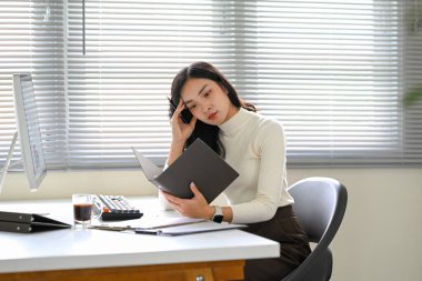 Hüsrana uğramış iş kadını, ofis masasındaki belgeleri incelerken bunalmış hissediyor..