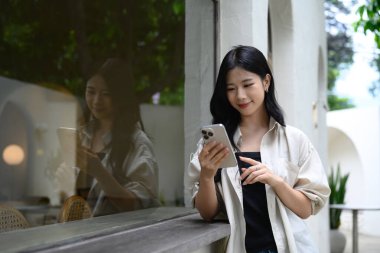 Kafe duvarına yaslanırken cep telefonunda gezinen şık bir kadın..