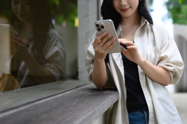 Kafe penceresinde yansıması olan akıllı telefon kullanan Asyalı genç bir kadın..