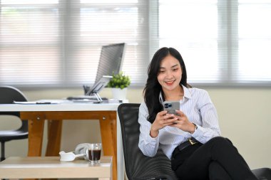 Asyalı ofis çalışanı, akıllı telefonunu kullanarak ofiste dinlenmekten zevk alıyor..