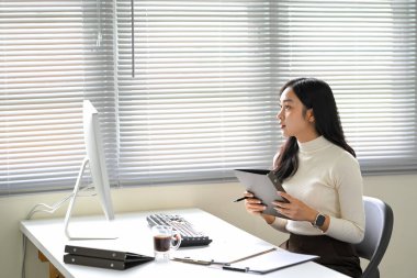Kadın ofis çalışanı modern bir çalışma alanında düşünceli bir şekilde görevler planlıyor ve düzenliyor..