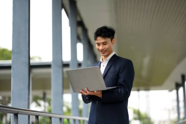 Ofis binasının dışında dizüstü bilgisayar kullanan kendine güvenen Asyalı iş adamı..