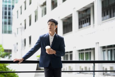 Kendine güvenen bir ofis çalışanı, elinde kahveyle modern bir şehir zeminine doğru mola veriyor..