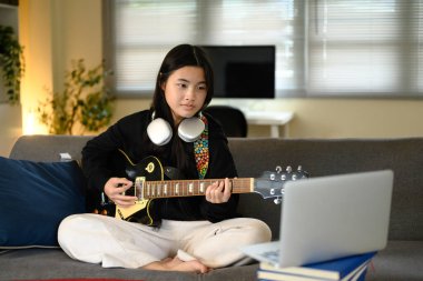 İnternette öğrenirken evde elektro gitar çalan genç kız..