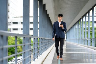 İş adamı akıllı telefonu kontrol ederken yaya köprüsünde güvenle yürüyor.