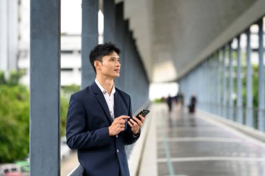 Kendine güvenen bir işadamı, elinde akıllı bir telefonla gökyüzünde duruyor ve kararlı bir şekilde bakıyor...