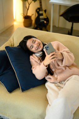 Genç kız kanepede uzanıyor, telefonuyla sosyal medyada geziniyor..