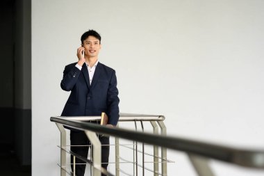 Kendine güveni tam bir işadamı, modern parmaklıkların yanında dururken akıllı telefondan konuşuyor..