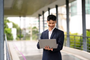 Açık havada dizüstü bilgisayar kullanarak resmi giyinmiş gülümseyen iş adamı..