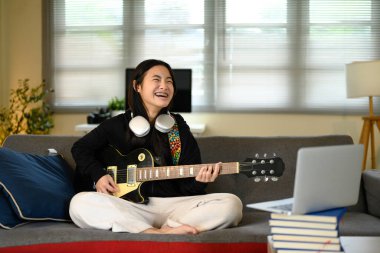 Online müzik seansı sırasında gitar çalan neşeli bir genç kız..