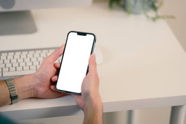 Modern bir masada boş beyaz ekranlı akıllı telefonu tutan ellerinizi kapatın..