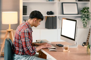 Genç adam evdeki masaüstü bilgisayarında çalışıyor, klavyeye odaklanarak daktilo ediyor..