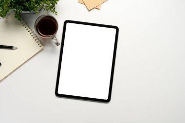 Kahve, not defteri ve bitkiyle birlikte beyaz masanın üzerinde düz bir tablet modeli var..
