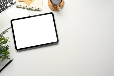 Temiz beyaz masa üzerinde boş ekranlı dijital tablet, bir dizüstü bilgisayar ve kahve fincanı ile çevrili..