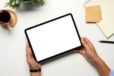 Eller temiz bir masada boş beyaz ekranlı dijital tableti tutuyor..