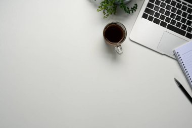 Dizüstü bilgisayarlı, minimalist çalışma alanı, bir fincan kahve ve temiz beyaz bir masanın üzerine not defteri..