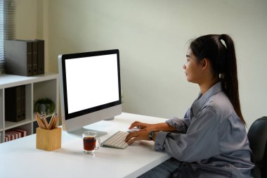 Masaüstü bilgisayarında beyaz ekranlı genç bir kadın modern bir ofiste oturuyor..