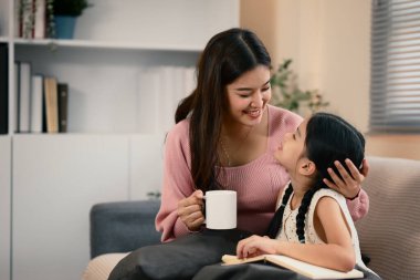 Kanepede kızıyla kaynaşırken elinde kahve fincanı tutan gülümseyen anne..