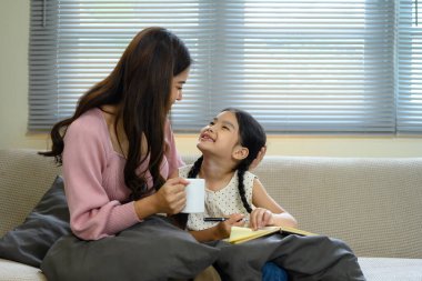 Gülümseyen anne ve kız kanepede oturup sıcak bir sohbetin tadını çıkarıyorlar..