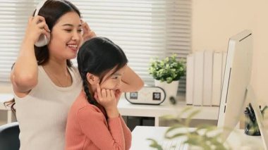 Gülümseyen anne ve genç kız rahat bir ofiste bilgisayarda birlikte çalışıyorlar..