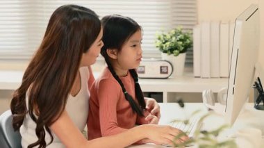 Parlak bir evde e-öğrenim ödevleri yaparak kızına rehberlik ediyor..