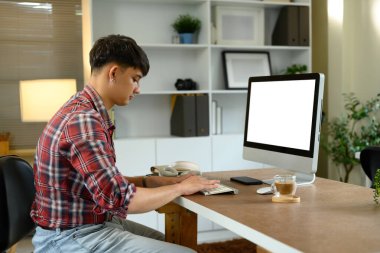 Masaüstü bilgisayarında ahşap masada kahve fincanıyla çalışan adamın yan görüntüsü..