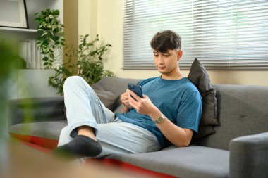 Rahat beyaz erkek kanepede oturuyor ve evde akıllı telefon kullanıyor..