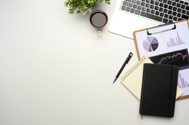 Ofis masasında dizüstü bilgisayarı, finansal tabloları, defterleri ve beyaz arka planda kahvesi olan düz bir masa..