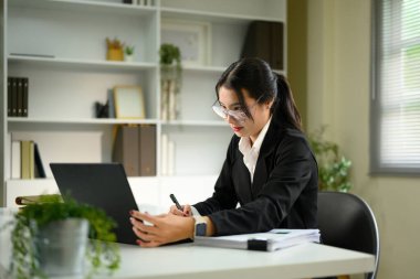 Modern bir masada not alırken dizüstü bilgisayarda çalışan odaklanmış bir iş kadını..