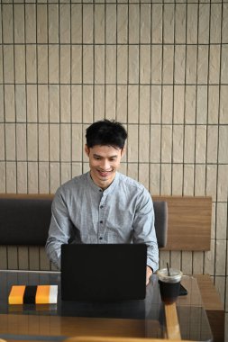 Modern bir kafe masasında dizüstü bilgisayarda çalışan genç Asyalı bir adam. İçki ve not defteriyle..