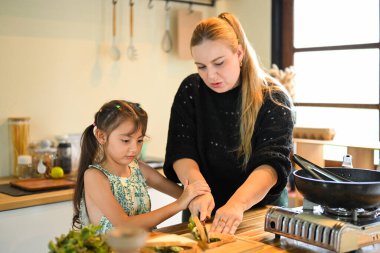Anne, kızının mutfak tezgahında yemek kesmesine yardım ediyor..