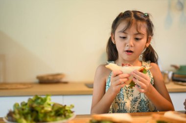 Genç kız elinde merakla taze yapılmış bir sandviçle mutfakta bir ısırık almaya hazırlanıyor..