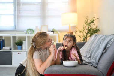 Anne ve kızı sıcak bir oturma odasında abur cubur yiyip kaynaşıyorlar..