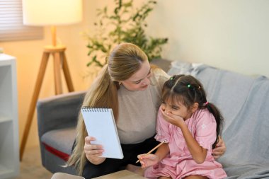 Mutlu anne küçük kızına ödevlerinde yardım ediyor, eğlenceli ve ilgi çekici bir anı paylaşıyor..