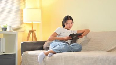 Evdeki bir kanepede dinlenen bir kadın dijital tableti tarama ya da eğlence için kullanıyor..