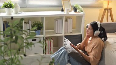 Kulaklıklı, müzikten hoşlanan ve akıllı telefon kullanan Asyalı genç bir kadın..