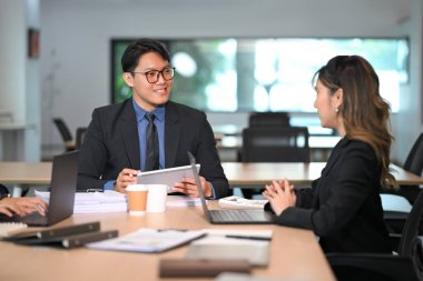 Modern bir ofiste bayan bir meslektaşla konuşurken elinde dijital tabletle gülümseyen bir işadamı..