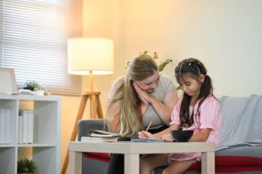 Bakıcı anne, küçük kızına ev ödevinde yardım ediyor..