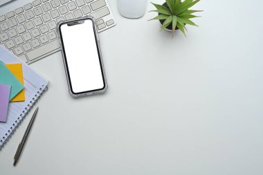 Boş telefon ekranı, kırtasiye malzemesi ve modern minimalist tarzı içeren çalışma alanı kurulumu.