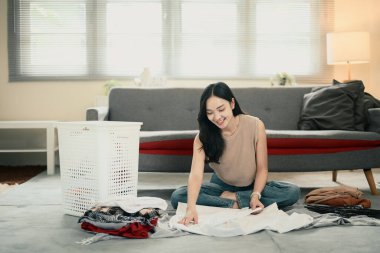 Gülümseyen Asyalı kadın evde yerde çamaşır katlıyor..
