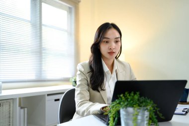 Modern ofis masasında dizüstü bilgisayarla çalışan bej ceketli odaklanmış iş kadını...