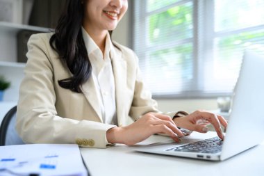 Modern ofis masasında dizüstü bilgisayarda yazan bej ceketli bir iş kadını..