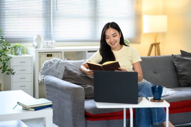 Kanepede rahat bir şekilde otururken uzaktan bilgisayarla çalışan serbest çalışan bir kadın..