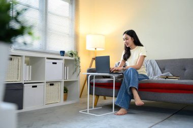 Kanepede oturan genç bir kadın evde dizüstü bilgisayarda çalışıyor, gündelik yaşam tarzı konsepti..