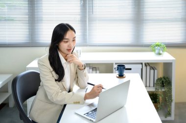 Blazer ceketli kendine güvenen bayan girişimci masasında iş planlaması için bilgisayar kullanıyor..