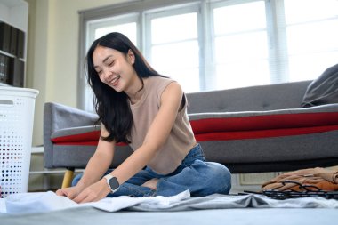 Neşeli kadın ev işlerini yapıyor, oturma odasında temiz kıyafetler düzenliyor..