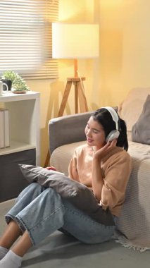 Genç Asyalı mutlu kadın kablosuz kulaklıklarla ses eğlencesinden hoşlanıyor..