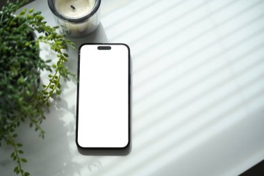 Boş ekran maketi ile akıllı telefon bitki ve mum ile beyaz masaya yerleştirildi.
